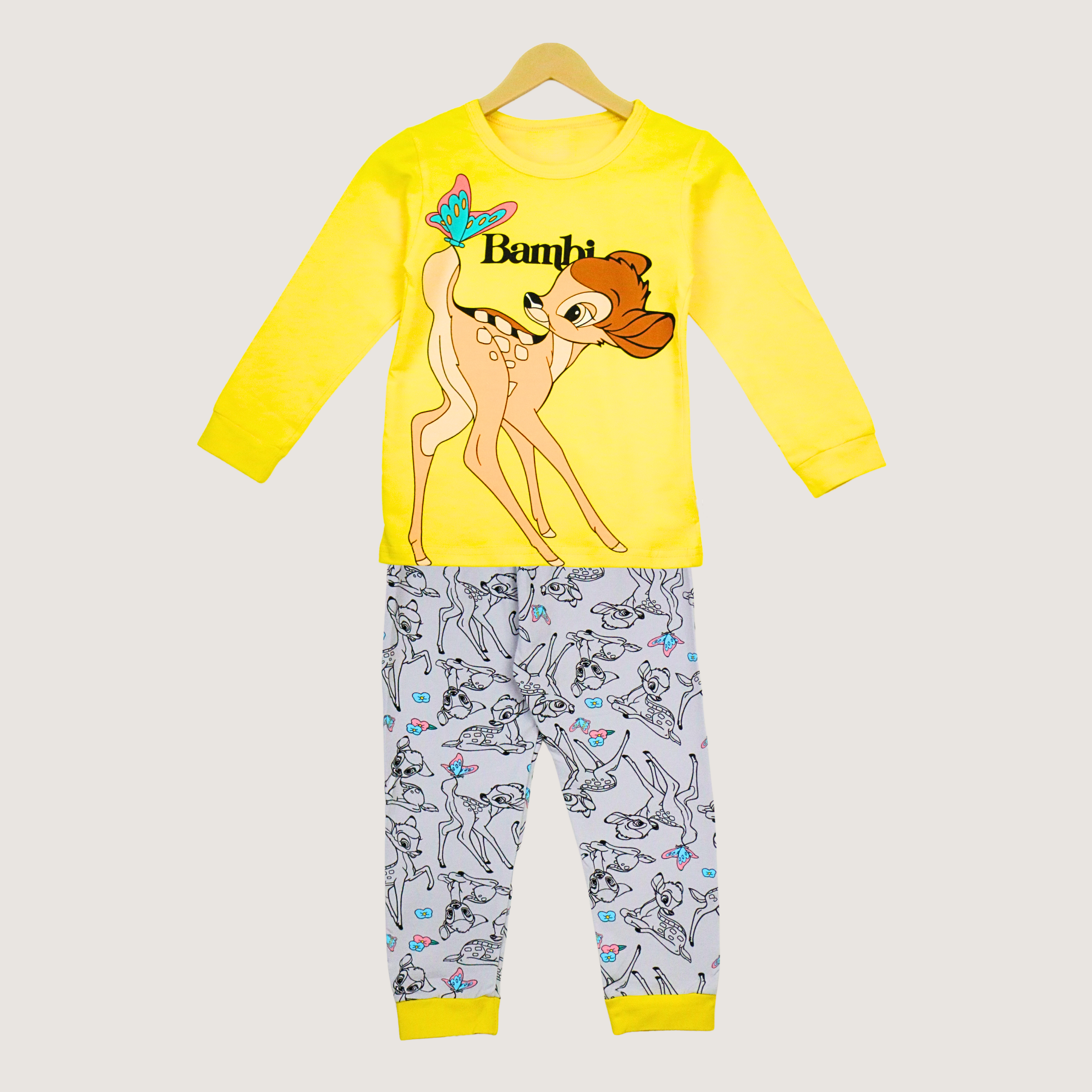 Children's pajama set with Bambi design on a yellow shirt and gray pants with character pattern, on a beige background.