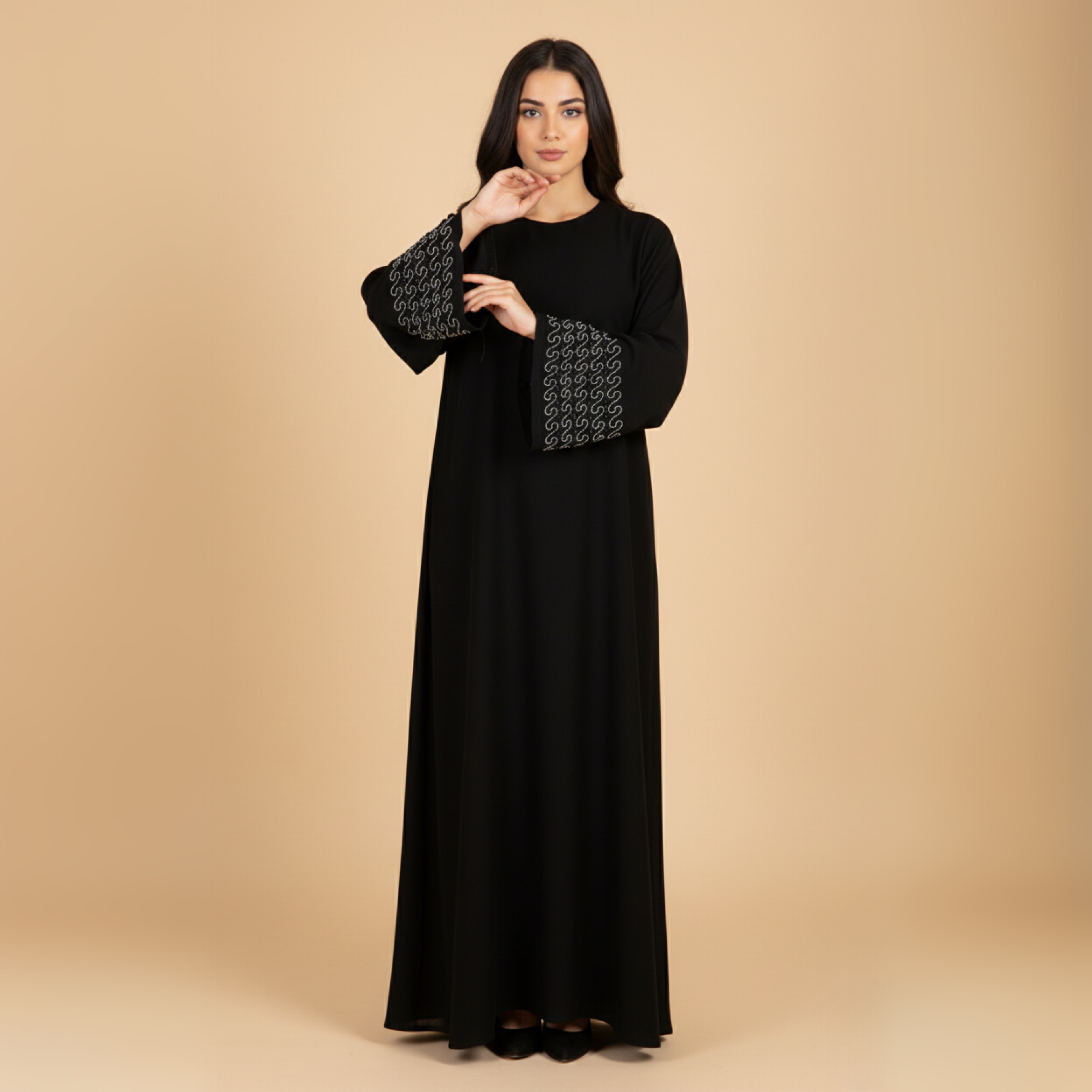 Woman wearing a black abaya with patterned cuffs on a beige background